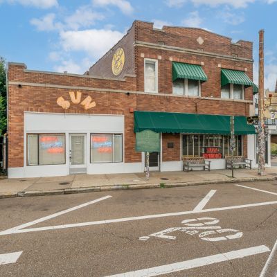 Street-level exterior of the historic Sun Studio brick building in the Edge District of Memphis, highlighting its signature green awnings, neon signs, and a giant vertical guitar landmark.