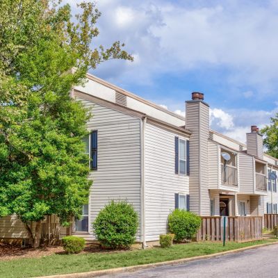 Street-level exterior view of Annie's Townhomes, a two-story North Memphis apartments community with beige siding, blue shutters, and mature shade trees