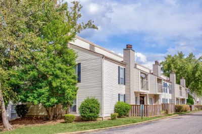 Street-level exterior view of Annie's Townhomes, a two-story North Memphis apartments community with beige siding, blue shutters, and mature shade trees
