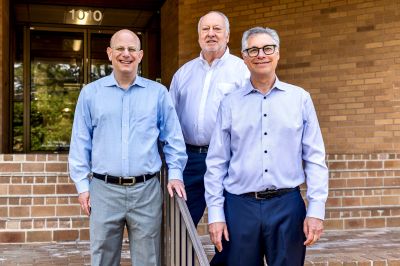 Three male executive owners of a Memphis apartments management company smiling together outside their office building