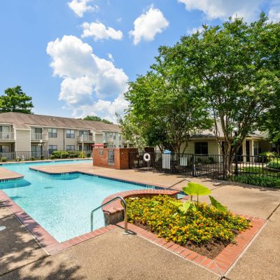 Outdoor swimming pool with brick surround and flowering garden at The Ellington, a Southeast Memphis apartments community surrounded by mature trees
