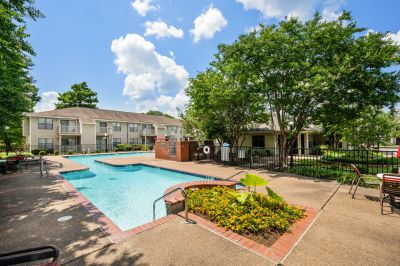 Outdoor swimming pool with brick surround and flowering garden at The Ellington, a Southeast Memphis apartments community surrounded by mature trees