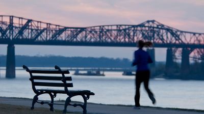 Person jogging along the Mississippi River at dusk near Downtown Memphis, with a historic bridge silhouetted against a pink and blue sunset sky