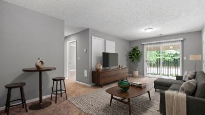 Virtually staged living room layout with a grey sectional, a wooden media console, and a sliding glass patio door at Annie's Townhomes and Apartments in Memphis.