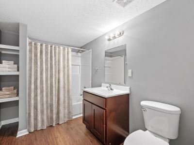 Staged bathroom complete with a dark wood vanity, linen shelving organizer, wood-style floors, and a modern shower curtain at Annie's Townhomes and Apartments in Memphis.