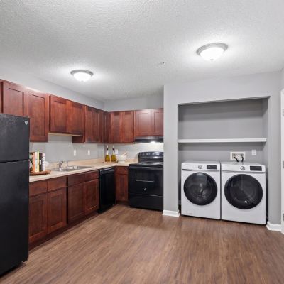 Staged kitchen showing dark espresso cabinets, black appliances, wood-look flooring, and a laundry alcove with a washer and dryer at Annie's Townhomes and Apartments in Memphis.