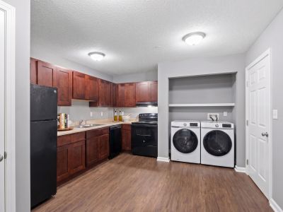 Staged kitchen showing dark espresso cabinets, black appliances, wood-look flooring, and a laundry alcove with a washer and dryer at Annie's Townhomes and Apartments in Memphis.