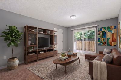 Virtually staged living room featuring a brown leather sectional, a mid-century media console, and a sliding glass door patio entrance at Annie's Townhomes and Apartments in Memphis.