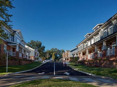Tree-lined interior street at The Park Memphis apartments community with brick and siding townhome-style buildings, covered porches, and a resident walking a dog