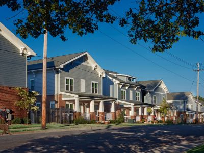 Streetscape view of a row of craftsman-style townhome Memphis apartments with brick and gray siding exteriors, covered entry porches, and mature shade trees