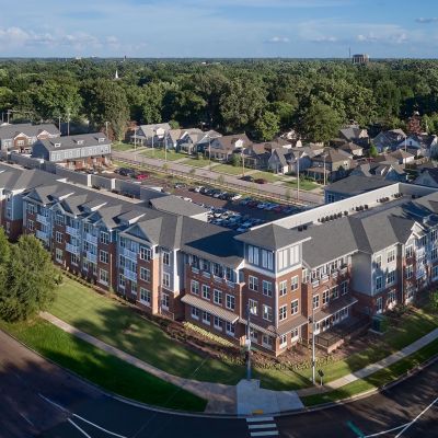 Aerial view of The Park Memphis apartments complex showing a large four-story brick building, adjacent townhomes, parking areas, and surrounding tree canopy
