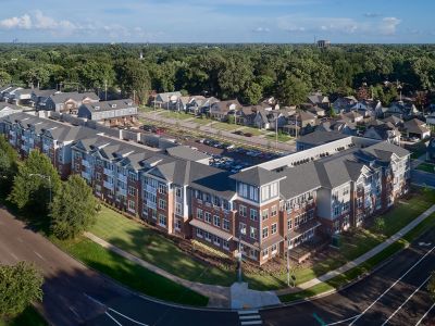 Aerial view of The Park Memphis apartments complex showing a large four-story brick building, adjacent townhomes, parking areas, and surrounding tree canopy