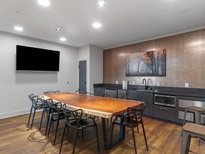Private dining and event room at The Park Memphis apartments featuring a live-edge wood communal table, modern chairs, wall-mounted TV, and a wet bar with dark cabinetry