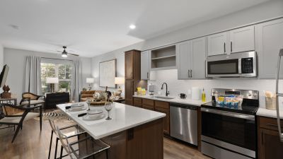 Open-plan kitchen and living area in a Memphis apartments unit at The Park, with quartz island, two-tone cabinetry, stainless appliances, and a furnished living room beyond