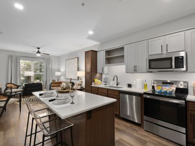 Open-plan kitchen and living area in a Memphis apartments unit at The Park, with quartz island, two-tone cabinetry, stainless appliances, and a furnished living room beyond