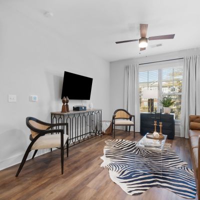 Furnished living room in a Memphis apartments unit at The Park featuring hardwood floors, ceiling fan, wall-mounted TV, and sliding glass door leading to natural light