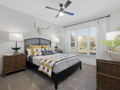 Spacious carpeted bedroom in a Memphis apartments unit at The Park with ceiling fan, large windows, upholstered bed with yellow and gray bedding, and wooden nightstands
