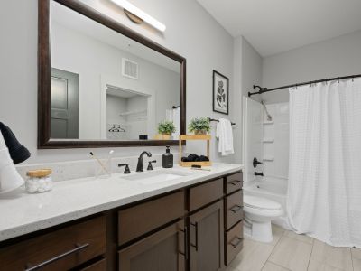 Full bathroom in a Memphis apartments unit at The Park featuring a dark-framed vanity mirror, quartz countertop, dark wood cabinetry, and shower-tub combo with white curtain