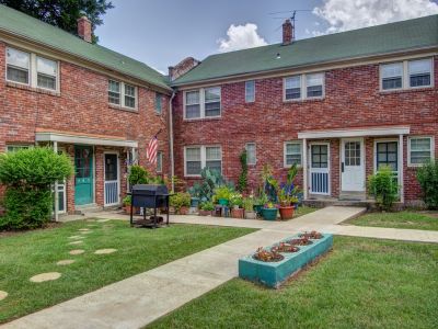 Charming brick courtyard area with individual apartment entry doors, potted plants, and a barbecue grill at Audubon Downs apartments in Memphis.