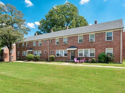 Traditional multi-family red brick apartment buildings surrounded by open green grass fields and mature trees at Audubon Downs apartments in Memphis.