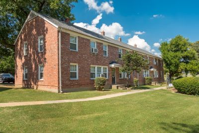 Two-story red brick residential building alongside a concrete walkway and green lawn at Audubon Downs apartments in Memphis.