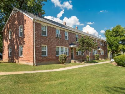 Two-story red brick residential building alongside a concrete walkway and green lawn at Audubon Downs apartments in Memphis.
