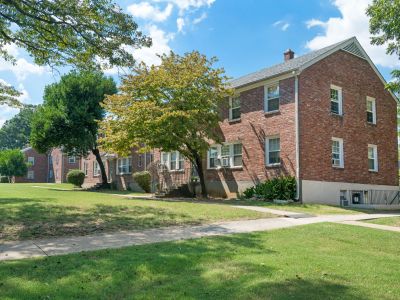 Exterior view of classic two-story brick apartment structures framed by shaded leafy trees and lawns at Audubon Downs apartments in Memphis