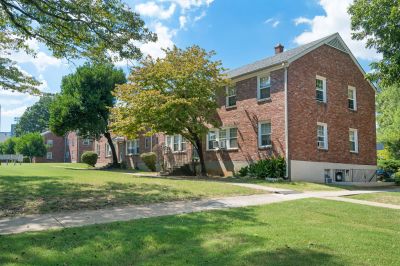 Exterior view of classic two-story brick apartment structures framed by shaded leafy trees and lawns at Audubon Downs apartments in Memphis