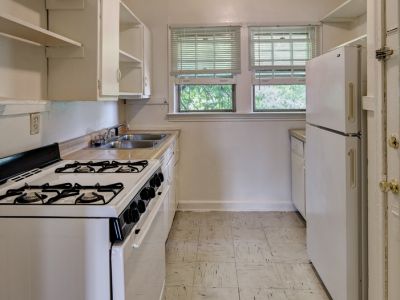 Galley kitchen with white appliances and cabinets on tile flooring at Audubon Downs apartments in Memphis