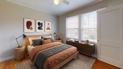 Virtually staged bedroom with hardwood floors, a light oak bed frame, rust-colored bedding, and modern lamps at Audubon Downs apartments in Memphis.