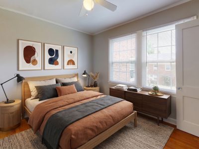 Virtually staged bedroom with hardwood floors, a light oak bed frame, rust-colored bedding, and modern lamps at Audubon Downs apartments in Memphis.