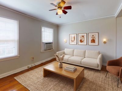 Staged living room with high-quality hardwood floors, a cream sectional sofa, a wooden coffee table, and an accent chair at Audubon Downs apartments in Memphis.