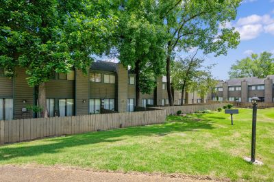 Exterior view of multi-level townhome buildings with brown siding, shaded by mature trees, and private wooden fences enclosing back patios at The Birches Townhomes in South Memphis.