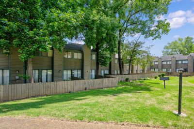 Exterior view of multi-level townhome buildings with brown siding, shaded by mature trees, and private wooden fences enclosing back patios at The Birches Townhomes in South Memphis.