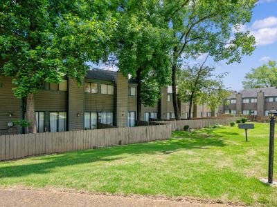 Exterior view of multi-level townhome buildings with brown siding, shaded by mature trees, and private wooden fences enclosing back patios at The Birches Townhomes in South Memphis.