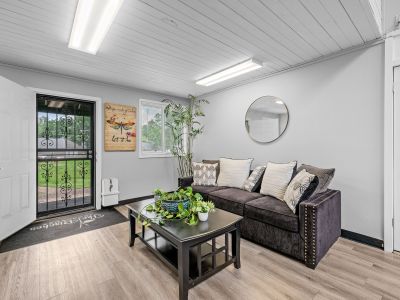 Comfortable resident lounge area featuring a dark sofa with patterned throw pillows, wood-look flooring, and an open front entry door at The Birches Townhomes in South Memphis.