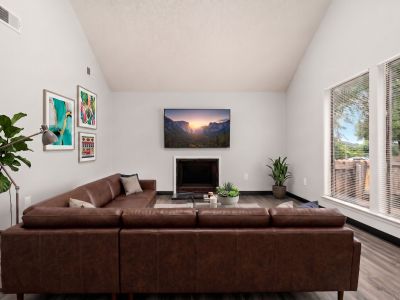 Virtually staged living room showing a modern brown leather sectional sofa, a fireplace, and a mounted flat-screen TV at The Birches Townhomes in South Memphis