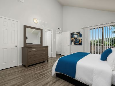 Virtually staged bedroom layout with wood-style flooring, a dark wood dresser with a mirror, and a bed accented with a vibrant blue throw at The Birches Townhomes in South Memphis.