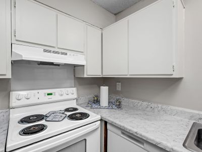 Close-up of a white electric range stove and matching range hood surrounded by white cabinets and marble-style countertops at The Birches Townhomes in South Memphis.