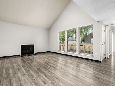 Unfurnished living room with a vaulted ceiling, a black fireplace, and three large windows overlooking a fenced backyard at The Birches Townhomes in South Memphis.