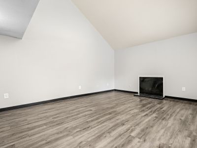 Wide-angle view of an empty living room highlighting the high vaulted ceiling, grey wood-style floors, and a corner fireplace at The Birches Townhomes in South Memphis.