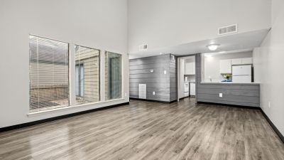 Open-concept unfurnished living area featuring grey wood-look floors, floor-to-ceiling windows, a grey paneled accent wall, and a kitchen view at The Birches Townhomes in South Memphis