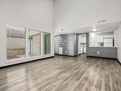 Open-concept unfurnished living area featuring grey wood-look floors, floor-to-ceiling windows, a grey paneled accent wall, and a kitchen view at The Birches Townhomes in South Memphis