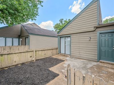 Private fenced rear patio featuring a concrete pad, a fresh mulch bed, and a dark green accent door at The Birches Townhomes in South Memphis.