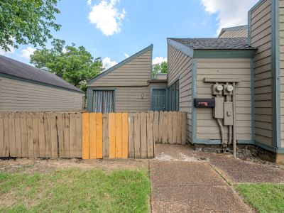 Exterior entry path showing building utilities on beige siding next to a wooden fence with planks at The Birches Townhomes in South Memphis