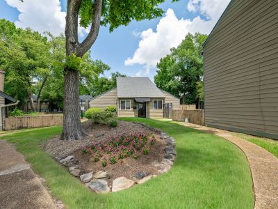 Manicured landscape feature showcasing a stone-lined oval flower bed filled with purple blossoms beneath a mature shade tree at The Birches Townhomes in South Memphis