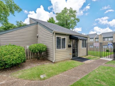 Exterior view of the leasing office building at address 1466, featuring a dark fabric awning, neat green bushes, and a black metal fence at The Birches Townhomes in South Memphis.