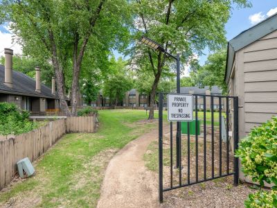 An open black metal security gate displaying a white sign that reads Private Property No Trespassing, opening onto a concrete path at The Birches Townhomes in South Memphis.