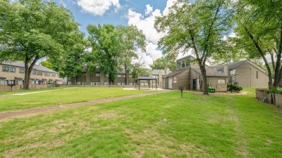 Wide-angle perspective of a massive open green courtyard lawn with a concrete walkway leading toward a distant gazebo at The Birches Townhomes in South Memphis.