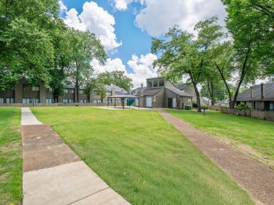 View of a large green courtyard lawn with concrete sidewalks splitting and leading toward a community building and gazebo at The Birches Townhomes in South Memphis.